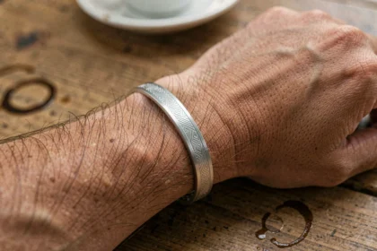 Bracelet homme gravure discrète motif géométrique en argent brossé porté au poignet sur une table en bois