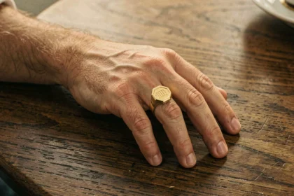 Chevalière en or pour homme portée à l'auriculaire, posée sur une table en chêne sombre, détail artisanal fabriqué en France